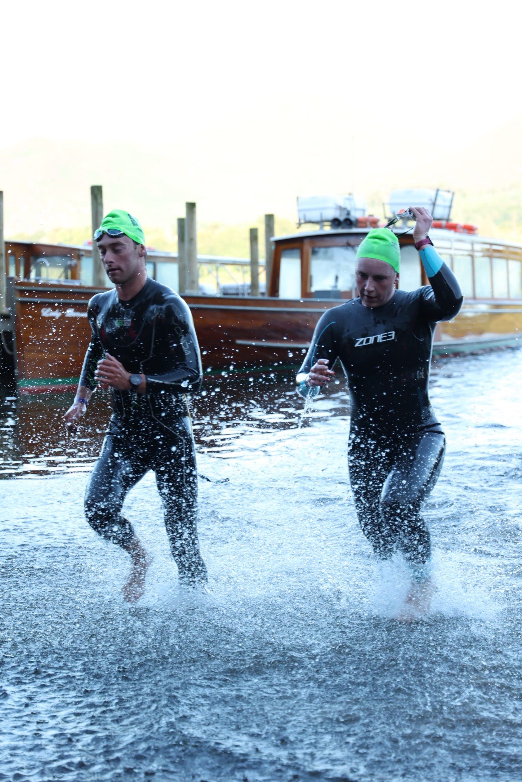 Triathletes in wetsuits running out of the water at the Lakesman swim exit