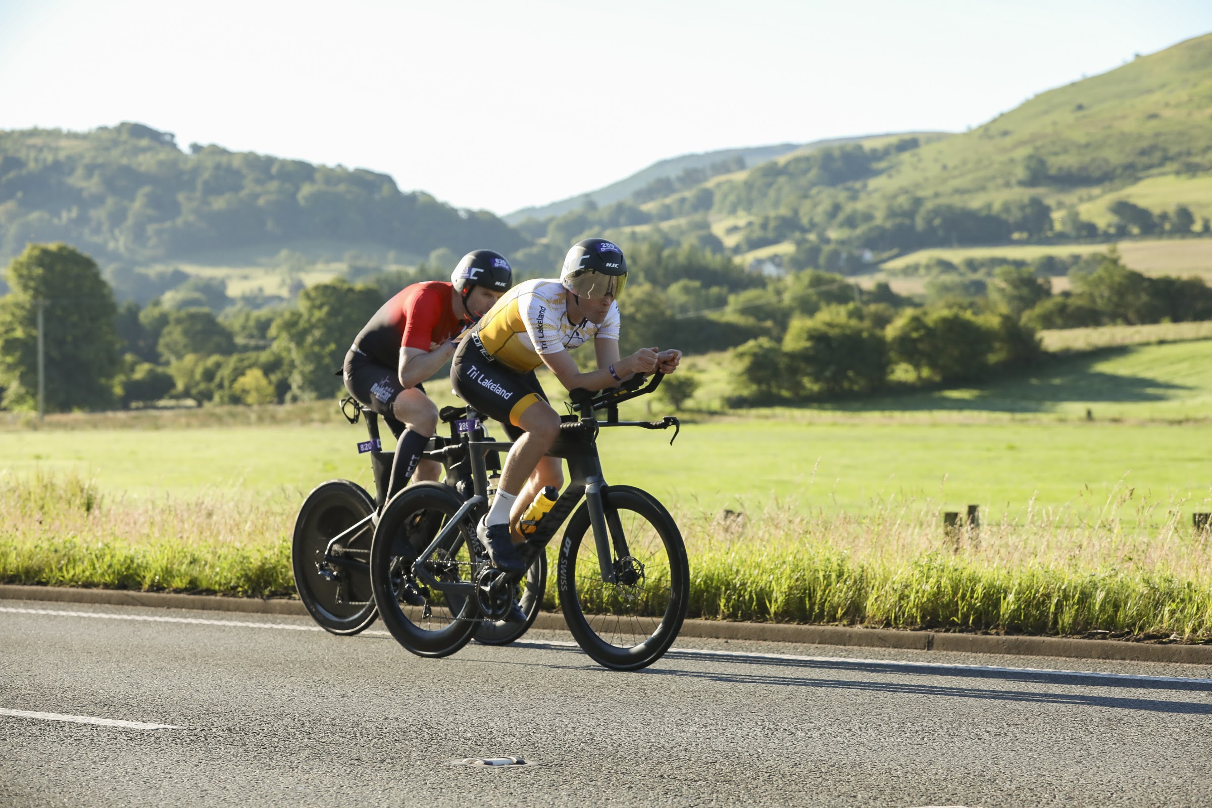 Cyclists on time-trial bikes on the Lakesman bike course with the Lake District fells behind
